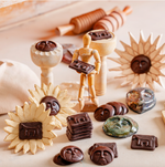 Celebrate! vegan chocolate sculpture set featuring face-shaped chocolates, sunflower molds, and symbolic square tiles, styled with wooden tools and mannequin on a light surface