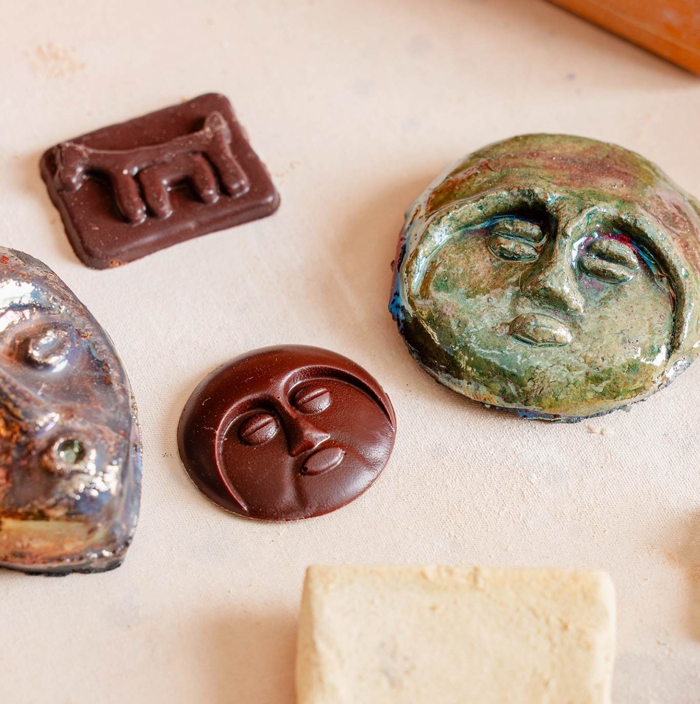 Celebrate! handcrafted sculpture set featuring moon face and creature designs in chocolate, clay, and metallic finishes, arranged on a light surface for expressive display