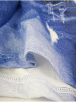 Close-up of blue denim fabric with a distressed white patch and visible stitching details.