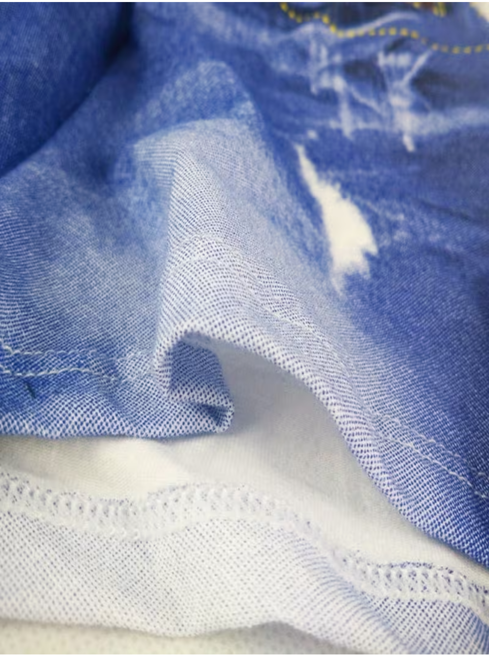 Close-up of blue denim fabric with a distressed white patch and visible stitching details.