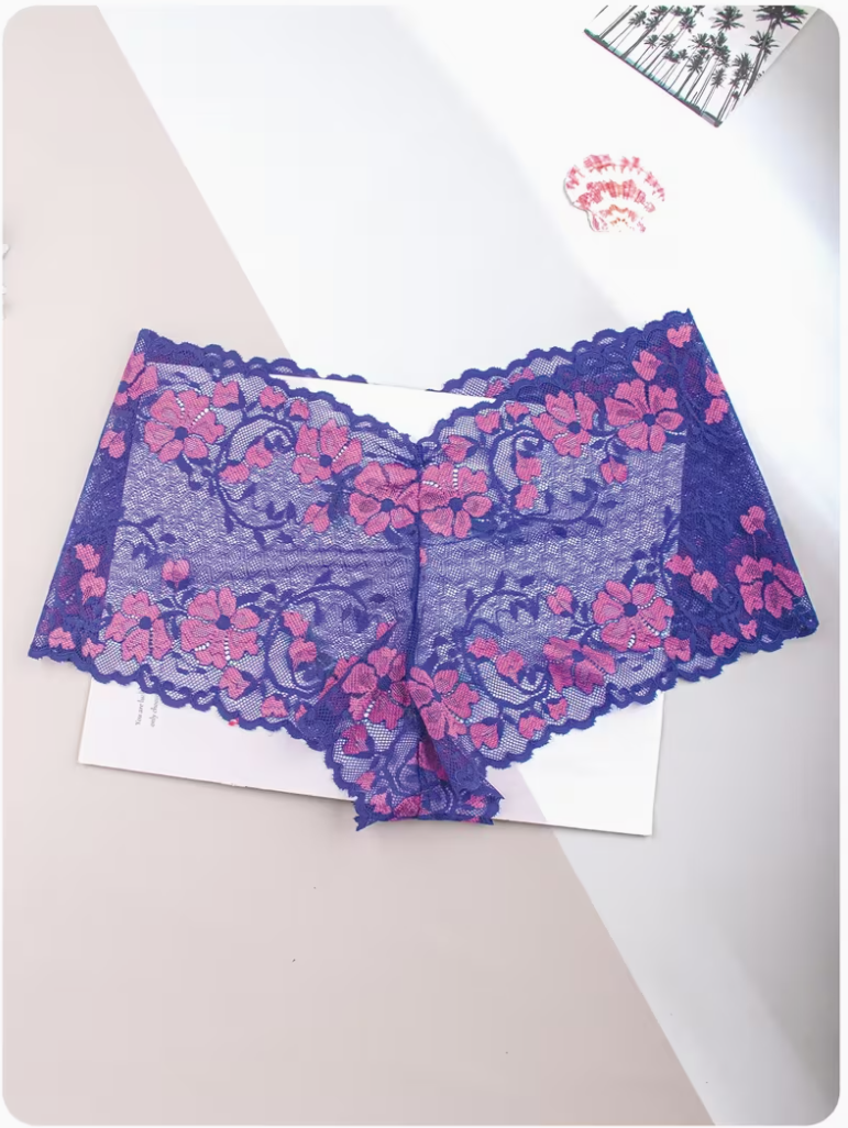 Purple lace underwear with pink floral embroidery, laid flat on a white card over a beige and white background.