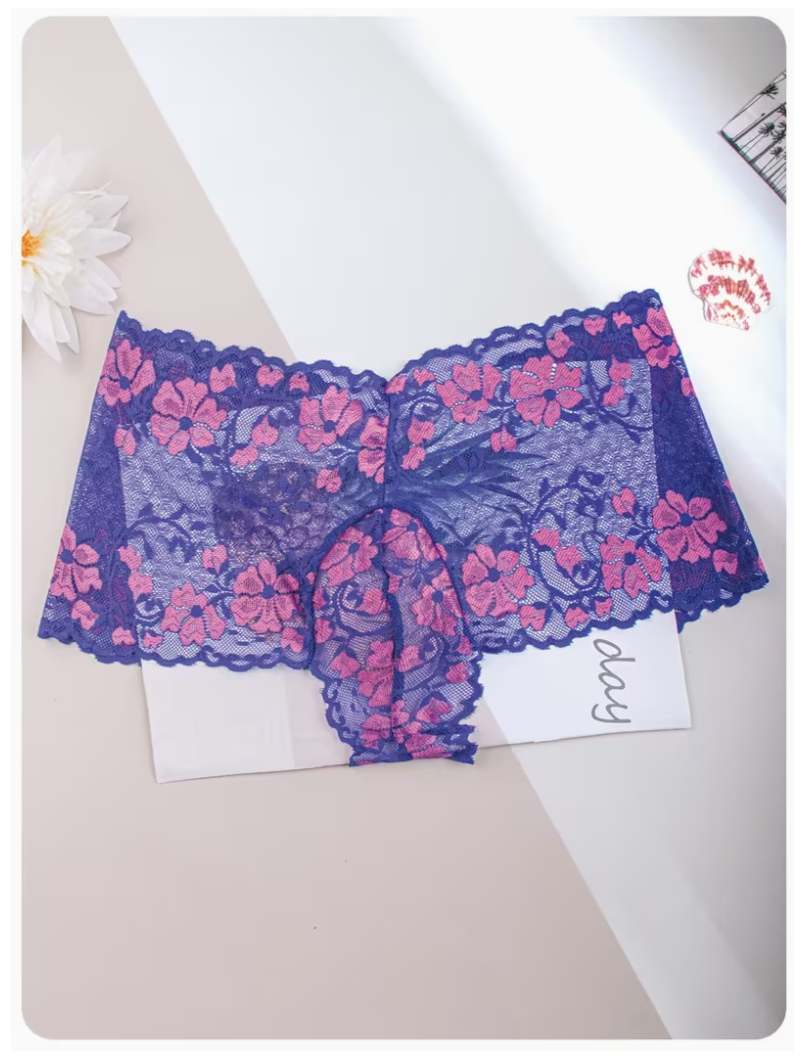 Blue lace panties with pink floral embroidery, laid flat on a white card over a beige and white background with a flower prop.