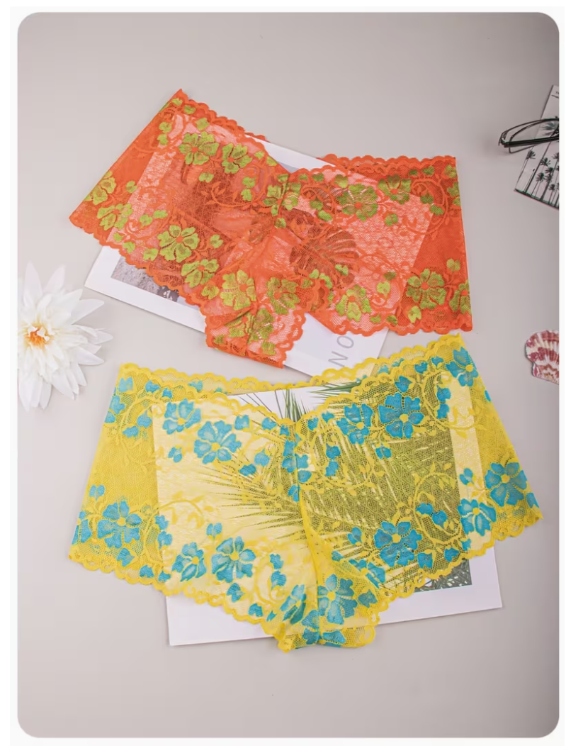 Two pairs of sheer floral lace panties laid flat on a light gray surface. The top pair is bright orange with green floral lace overlay, and the bottom pair is yellow with blue floral lace overlay.